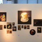 artrmx e. V. | Atelierzentrum Ehrenfeld Verschiedene Kunstwerke hängen leicht ungleichmäßig an einer weißen Wand in einer Galerie.Various works of art hang slightly unevenly on a white wall in a gallery.