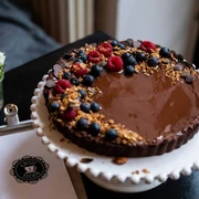 Cafe Adeli Schokoladenkuchen mit Beeren und Streuseln auf Tortenteller, im Hintergrund Blumen und Menükarte.Chocolate cake with berries and sprinkles on a cake plate, flowers and menu card in the background.