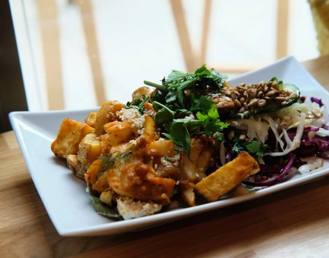 Sattgrün Ein rechteckiger Teller mit einer ansprechend angerichteten vegetarischen Mahlzeit. Links auf dem Teller befinden sich knusprig gebratene Tofu-Stücke, garniert mit einer Kräutersauce. Rechts ist ein knackiger, bunter Salatmix aus Rotkohl, Weißkohl, Rucola und Sonnenblumenkernen zu erkennen, der frisch und farbenfroh wirkt.A rectangular plate attractively arranged with a vegetarian meal. On the left side are crispy fried tofu pieces garnished with an herbal sauce. On the right side is a crunchy, vibrant salad mix of red cabbage, white cabbage, arugula, and sunflower seeds, appearing fresh and colorful.