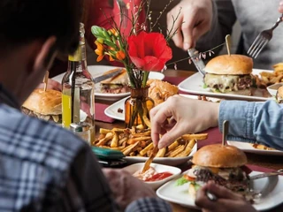 Die fette Kuh Burger Nahaufnahme von Tellern mit Burgern und Pommes. Eine Hand tunkt eine Pommes in Ketchup. Close-up of plates with burgers and fries. A hand dips a French fry into ketchup.