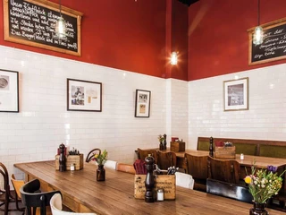 Die fette Kuh Rustikale Holztische in einem Raum mit weißen Fliesen und roten Wänden.Rustic wooden tables in a room with white tiles and red walls.