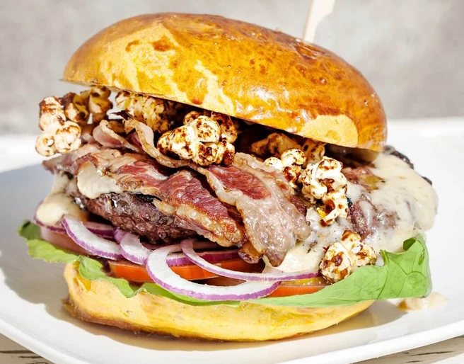 Die fette Kuh Burger Üppig belegter Burger mit Speck, Popcorn, Zwiebel, Salat und Patty.A burger with bacon, popcorn, onions, salad and a patty.