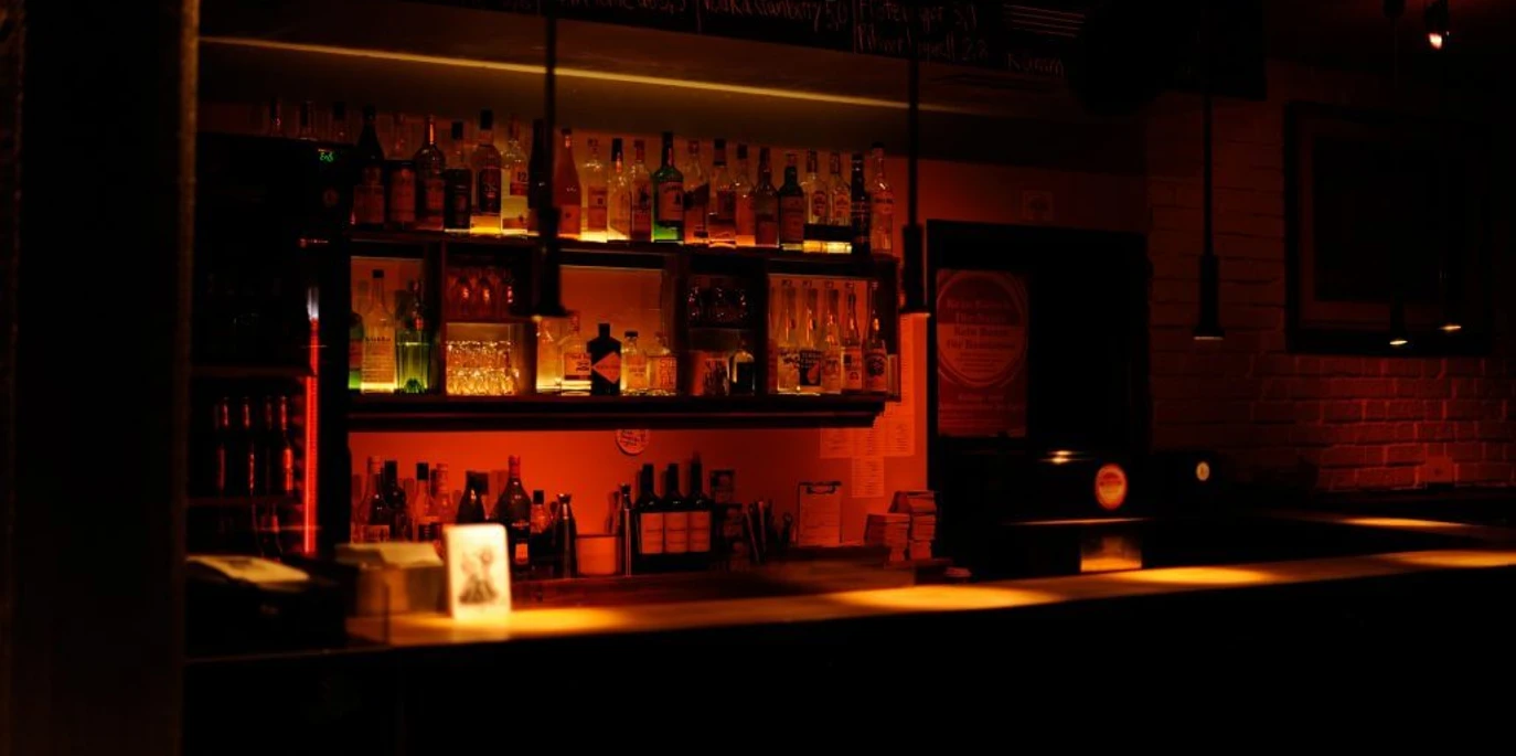Pegel Auf dem Bild zeigt sich eine stimmungsvoll beleuchtete Bar mit einer Reihe von Flaschen und Gläsern hinter dem Tresen. Warme Lichter schaffen eine einladende Atmosphäre.The picture shows an atmospherically lit bar with a row of bottles and glasses behind the counter. Warm lights create an inviting atmosphere.