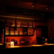 Pegel Auf dem Bild zeigt sich eine stimmungsvoll beleuchtete Bar mit einer Reihe von Flaschen und Gläsern hinter dem Tresen. Warme Lichter schaffen eine einladende Atmosphäre.The picture shows an atmospherically lit bar with a row of bottles and glasses behind the counter. Warm lights create an inviting atmosphere.
