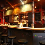 Lotta Bar Innenansicht auf den Barbereich. Die Theke ist schwarz lackiert und davor stehen Metallhocker. Interior view of the bar area. The counter is painted black and metal stools are placed in front of it.