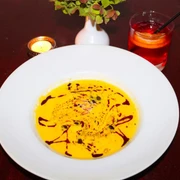 Traubenzeit Ein weißer Teller auf dunklem Tisch, gefüllt mit cremiger Suppe, dekoriert mit Ölspiralen und Samen.A white plate placed on a dark table, filled with creamy soup decorated with spirals of oil and sprinkled with seeds.
