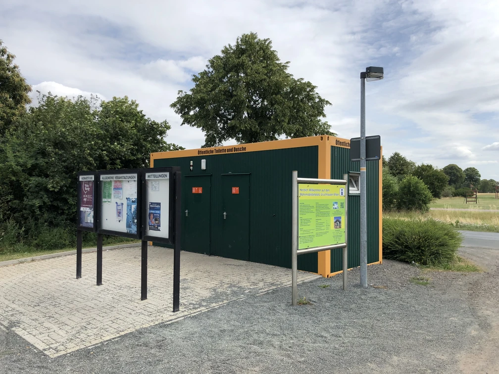Toilette am Wohnmobilstellplatz Bruchhausen-Vilsen Grüne Sanitäranlage an einem Wohnmobilstellplatz mit Informationsschild und gepflastertem Vorplatz.