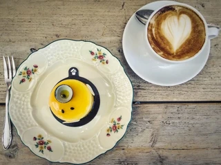 Törtchen Törtchen  Ein elegantes gelbes Törtchen auf feinem Porzellanteller neben einer Cappuccinotasse mit Herzmotiv.An elegant yellow tartlet served on a fine porcelain plate next to a cappuccino cup decorated with a heart motif.