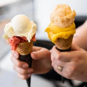 ice cream parlor Keiserlich Nahaufnahme, eine Person hält zwei Waffelhörnchen mit jeweils zwei Kugel Eis in die Kamera. Close-up of a person holding two waffle cones, each with two scoops of ice cream, up to the camera.