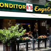 Konditorei Eis Engel Fassade mit Markise und in großen Buchstaben platziertes Schild über der Markise. Mensch sitzen vor der Konditorei.Facade with awning and sign placed in large letters above the awning. People sitting in front of the cafe.