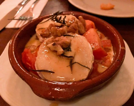 Tapeo and co Eine rustikale Tonschale gefüllt mit überbackenem Ziegenkäse, Tomaten, Walnüssen und Rosmarin.A rustic clay bowl filled with baked goat cheese, tomatoes, walnuts, and rosemary.