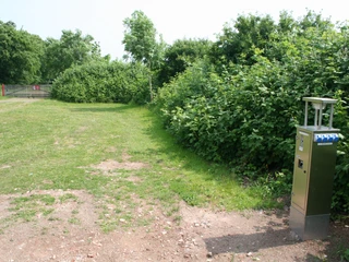 Wohnmobilstellplatz am Schloss Erbhof Wohnmobilstellplatz vor grüner Hecke und Bäumen, mit Stromsäule im Vordergrund auf Kiesboden.