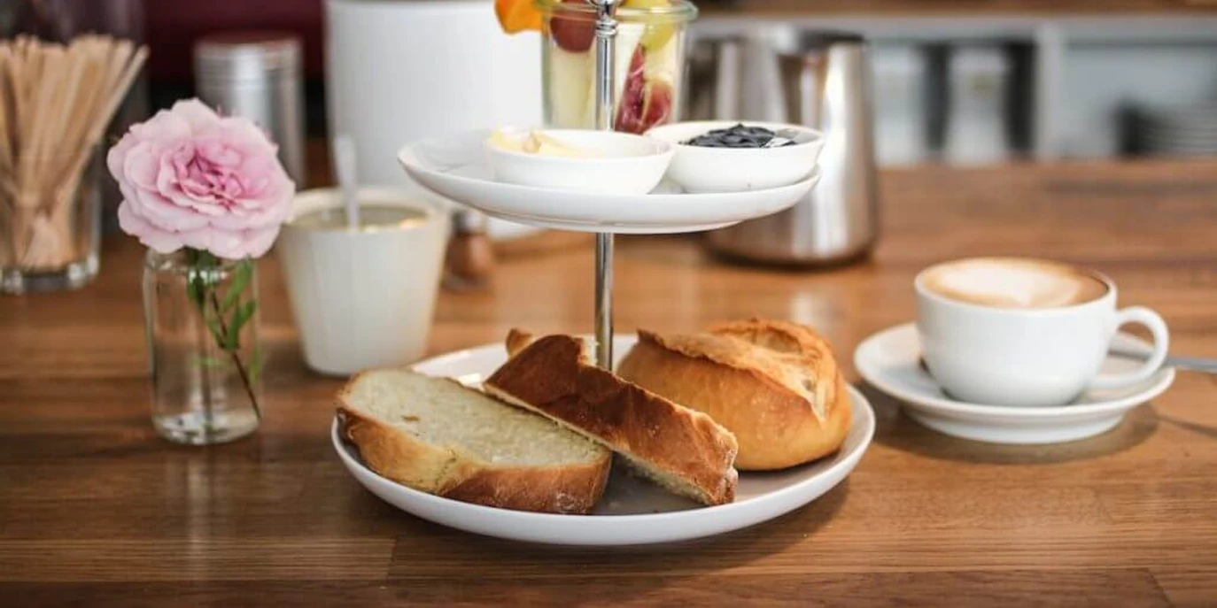 Cafe dein und mein Ein köstliches Frühstücksset mit frisch gebackenen Brötchen, Butter, Marmelade, Obst und Kaffee.A delicious breakfast set with freshly baked rolls, butter, jam, fruit and coffee.