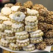 Simitzade Vielzahl von feinen Gebäckstücken, darunter mit Puderzucker bestäubte Kekse und mit Samen bedeckte Cookies auf einem Teller angerichtet.An assortment of delicate pastries arranged on a plate, including powdered sugar-dusted biscuits and cookies topped with seeds.