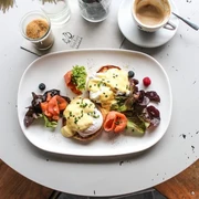 Hinz und Kunz Frühstücksteller mit Egg Benedict, Lachs, Salat und einem schwarzen Kaffee. Breakfast plate with egg benedict, salmon, salad and a black coffee.