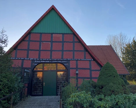 Katholische Kirche Windheim Ein traditionelles Fachwerkhaus mit rotem Ziegeldach und grünem Gartentor, umgeben von Bäumen.