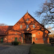 Mühlenbauhof Petershagen Historischer roter Backsteinbau mit steilem Dach, umgeben von Baum und gepflastertem Vorplatz.