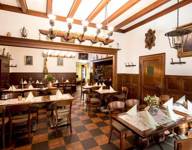 Restaurant Haus Scholzen Rustikal eingerichtetes Restaurant mit Holzbalken an der Decke und Bilder in goldenen Rahmen an den WändenRustic restaurant with wooden ceiling beams and paintings in golden frames on the walls