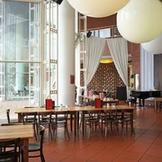 Café Restaurant Ludwig im Museum Großzügiger Restaurant Innenbereich mit bodenlanger Glasfront. Dunkle Holztische erschaffen eine Gemütlichkeit und an der Decke hängen riesige ballonähnliche Lampen.Spacious restaurant interior with floor-to-ceiling glass front. Dark wooden tables create a cozy atmosphere and huge balloon-like lamps hang from the ceiling.