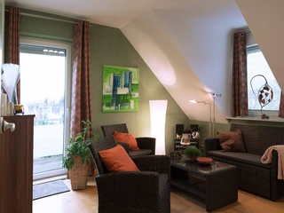 fewo-startpunkt1-lesezimmer.jpg Wohnzimmer einer Ferienwohnung unter Dachschräge mit modernen Rattanmöbeln und dekorativen Elementen.