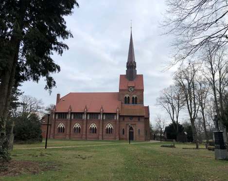Backsteinkirche St. Michaelis in Heemsen, umgeben von Bäumen auf einer großen, offenen Grünfläche.