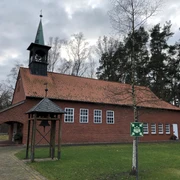 Kapelle Lichtenhorst Backsteinkapelle mit grünem Kirchturm, umgeben von Rasen und Bäumen, unter bewölktem Himmel.