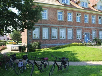 Amtshaus Westen Dreigeschossiges Backsteingebäude mit weißen Sprossenfenstern, Fahrräder im Vordergrund, blauer Himmel.