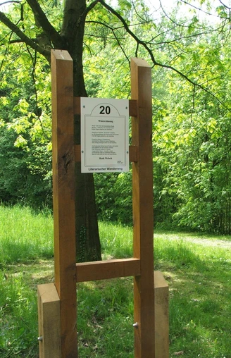Literarischer Wanderweg Hölzerne Infotafel Nummer 20 auf einem Wanderweg, umgeben von grünem Laub und sonnigem Licht.