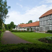 image Fachwerkgebäude mit roten Dächern neben einem gepflegten Garten mit Rasenfläche und Gehweg.