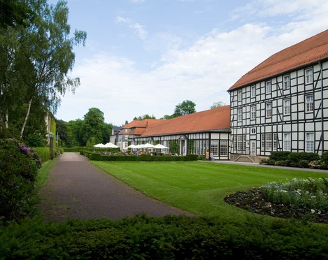 image Fachwerkgebäude mit roten Dächern neben einem gepflegten Garten mit Rasenfläche und Gehweg.