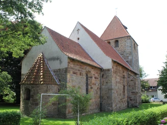Kirche Buchholz Eine historische Fachwerkkirche mit Steinfassade und roten Ziegeldächern, umgeben von Bäumen und Wiese.