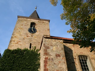 Historische Kirche Nendorf mit Uhrturm aus Backstein, umgeben von Herbstbäumen und klarem Himmel.