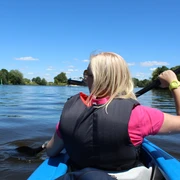 Kanutour Mittelweser Eine Frau paddelt in einem blauen Kanu auf einem ruhigen Fluss, umgeben von grüner Landschaft.