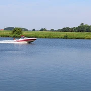 Ein schnelles Motorboot gleitet über die ruhige Weser, umgeben von grüner Landschaft und blauem Himmel.