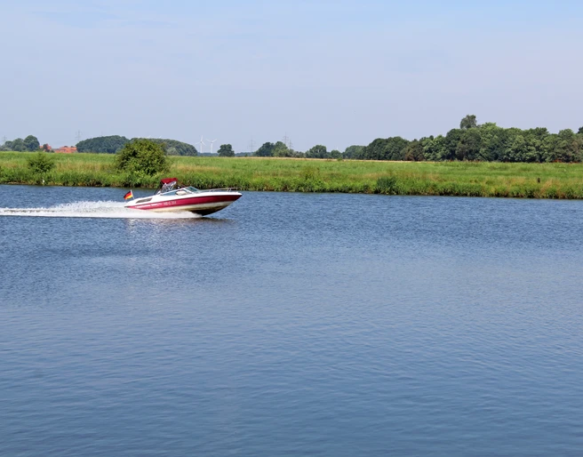 Dörverden Weser Ein schnelles Motorboot gleitet über die ruhige Weser, umgeben von grüner Landschaft und blauem Himmel.