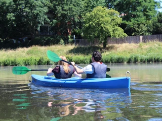 Kanutour Mittelweser Ein Paar paddelt in einem blauen Kanu gemächlich entlang eines Flusses, umgeben von üppigem Grün.