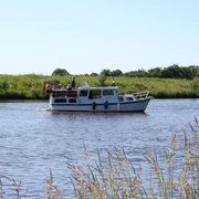 Boot auf Mittelweser Ein kleines Motorboot mit Personen fährt entlang eines ruhigen Flusses, umgeben von grüner Natur.