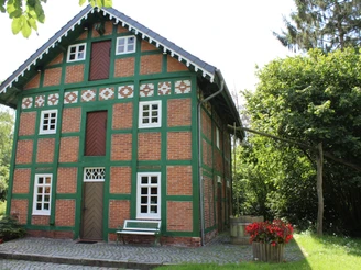 Spieker Lahausen Ein zweistöckiges Fachwerkhaus mit rot-grünen Backsteinen und weißen Fenstern umgeben von Bäumen.