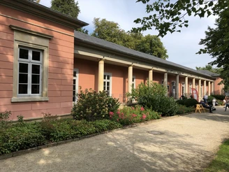 Rosafarbenes Gebäude in Bad Rehburg, umgeben von gepflegtem Garten und blauem Himmel im Hintergrund.