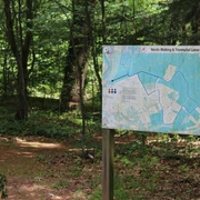 Nordic Walking und Trimpfad Leese Wegweiser im Wald mit Karte für Nordic Walking und Trimm dich Pfad Leese, umgeben von Bäumen und Laub.