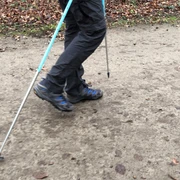 Nordic Walking Ein Nordic Walking-Enthusiast geht auf einem mit Herbstlaub bedeckten Pfad mit Trekkingstöcken.