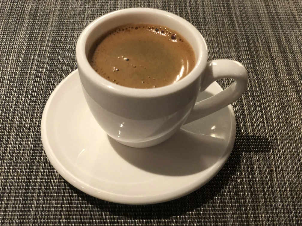 Espresso Eine weiße Espressotasse mit heißem, cremigem Espresso auf einem passenden Unterteller auf Stoffmatte.