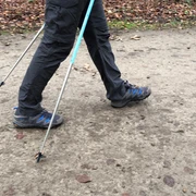 Nordic Walking Person auf Waldweg beim Nordic Walking mit Stöcken, herbstlicher Boden, Fokus auf Beine und Schuhe.