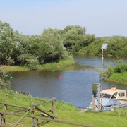 Ein Flussabschnitt mit einem Boot am Ufer, umgeben von grüner Vegetation und einem blauen Himmel.