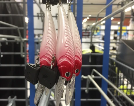 Angelhaken Drei kunstvolle Angelköder in rot-weiß mit Federmuster hängen an einer Metallhalterung in einem Geschäft.