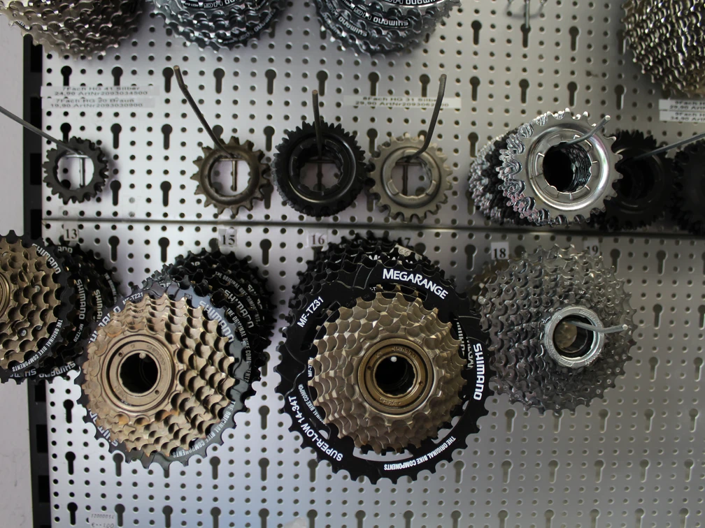 Verschiedene Fahrradritzel und Kassetten hängen geordnet an einer perforierten Metallwand.