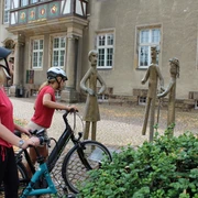 Familienskulptur Petershagen Zwei Radfahrer betrachten eine metallerne Skulpturengruppe in einer historischen Altstadt.