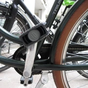 Ein schwarzes Fahrrad steht auf einem Betonboden; ein Pedal und die Kettenlöcher sind im Fokus.