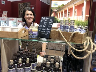 Früchtehof Schindler Frau hinter einem Stand bietet verschiedene Liköre und Honig in einer rustikalen Umgebung an.