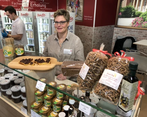 Bartels Hoff Ein Frau mit Brille steht an einem Verkaufsstand mit regionalen Produkten wie Honig und Teigwaren.